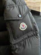 Black puffer jacket with round logo badge on sleeve and stitched paneling