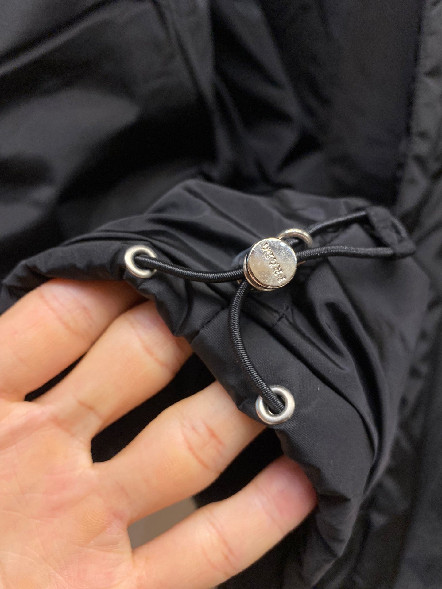 Prada long nylon jacket, dark color, close-up of drawstring toggle and cord ends