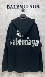 Black hoodie with white Balenciaga logo text on the back, hood up on a hanger