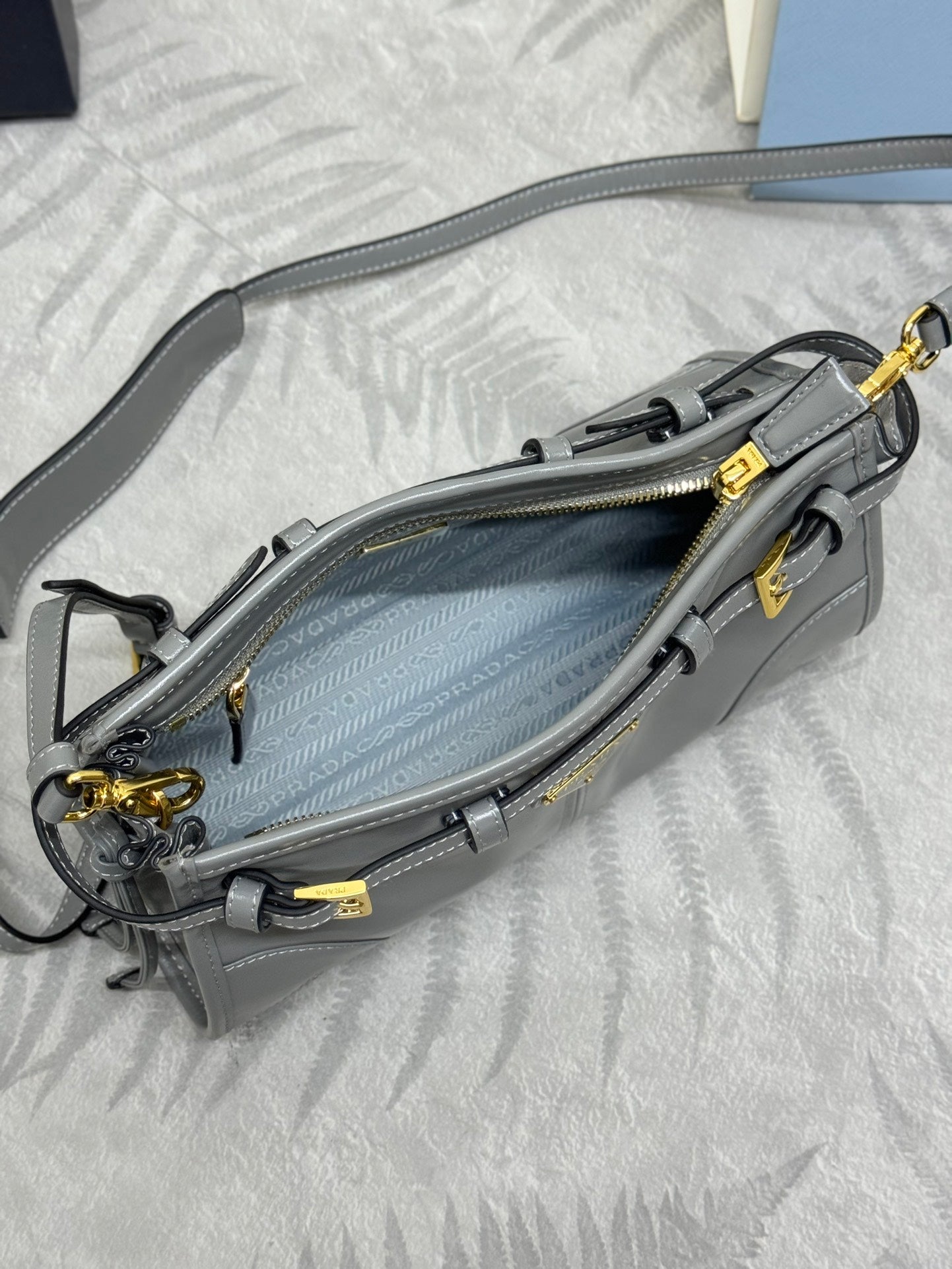 Light gray Prada bag open interior view with zipper closure, side pockets, and gold hardware.