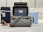 Light gray Prada bag in leather with crossbody strap, gold hardware, front logo plate.