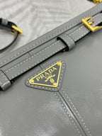 Prada bag strap close-up with gold buckle and triangular logo patch on gray leather.