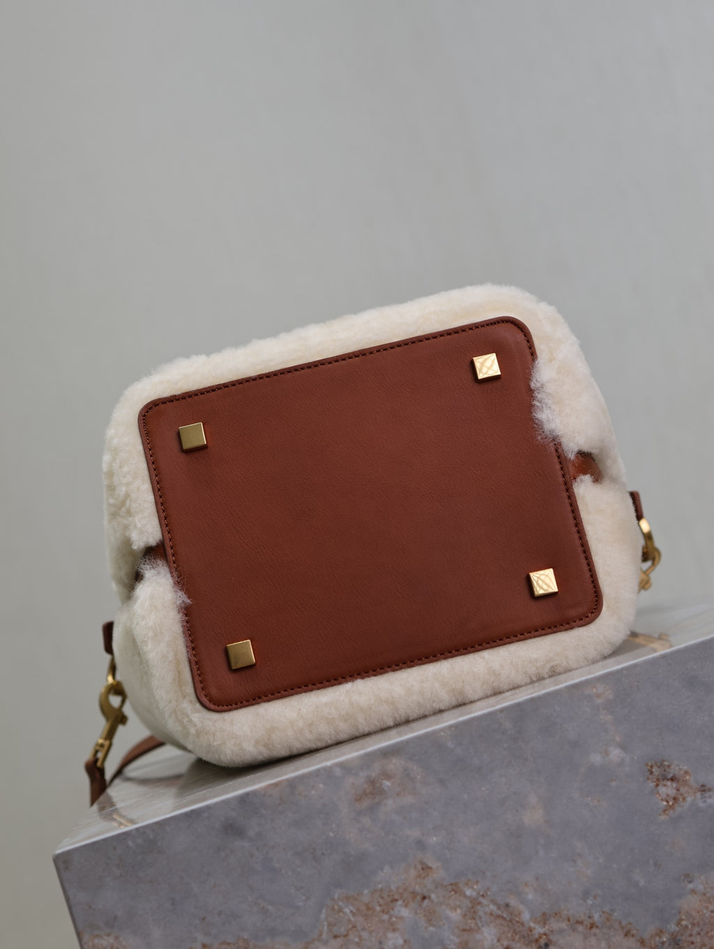 Brown leather-paneled YSL bag with cream shearling trim and gold corner studs