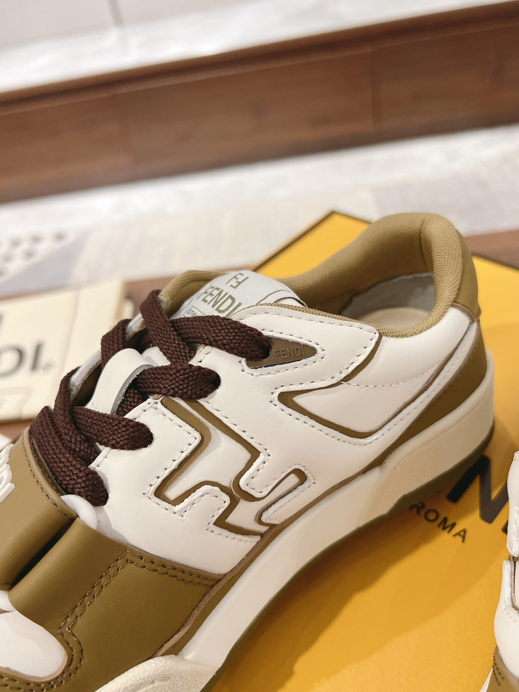 Fendi low-top sneakers close-up with white uppers, tan trim, and dark brown lace-up