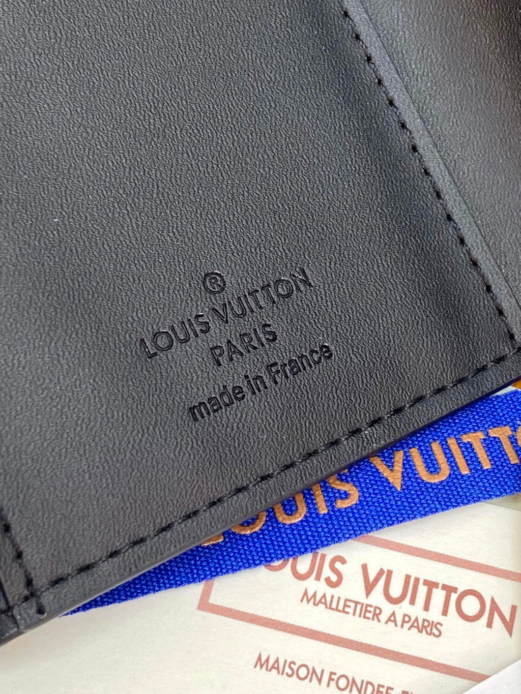 Small dark leather wallet close-up with stamped brand text and stitched edge