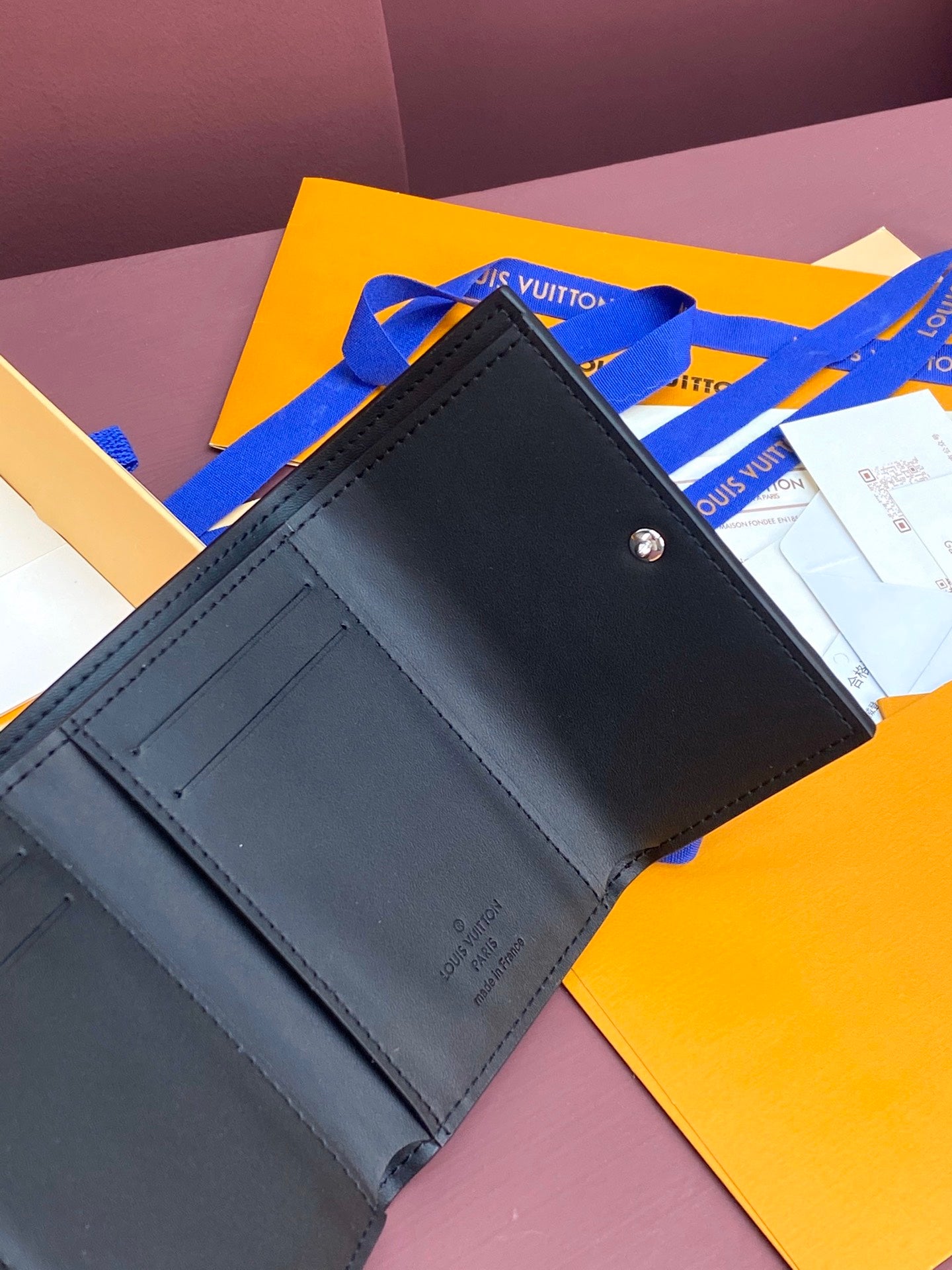 Small dark leather wallet with card slots, visible stitching and snap button