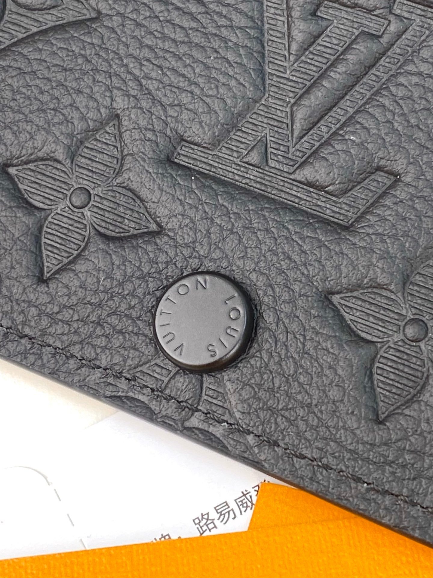 Small dark leather wallet close-up with embossed monogram details and snap button