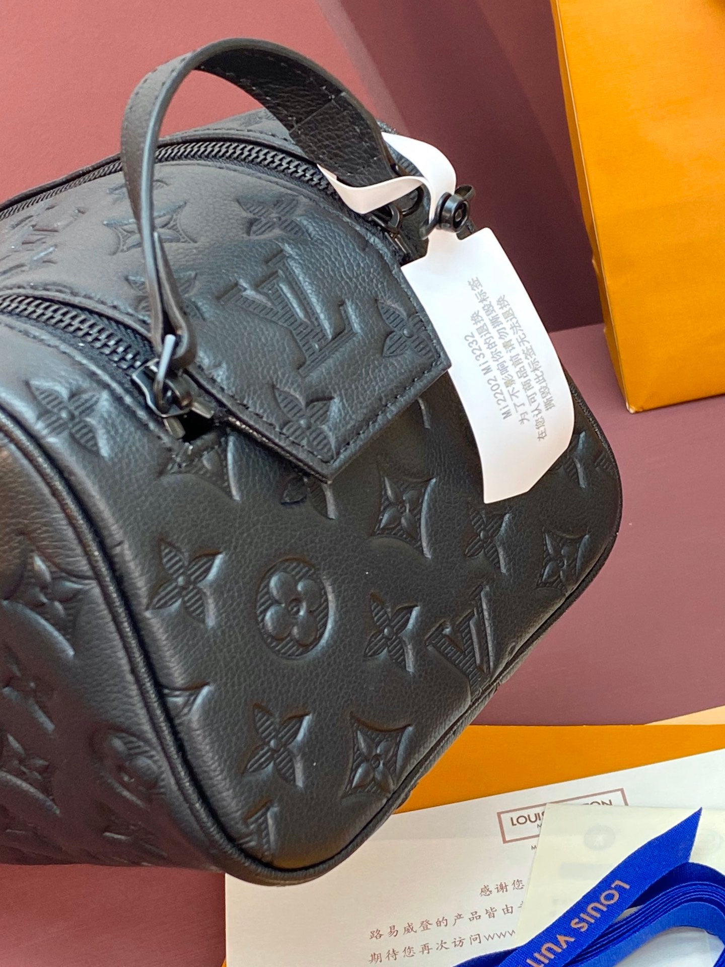 Close-up of embossed monogram toiletry bag with top handle and white hang tag