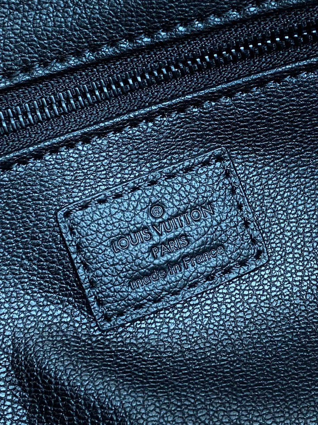 Close-up of embossed monogram leather label on toiletry bag with stitched edge