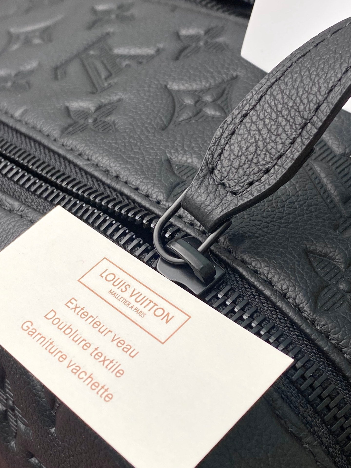 Close-up of zip track and leather pull tab with warranty tag on toiletry bag