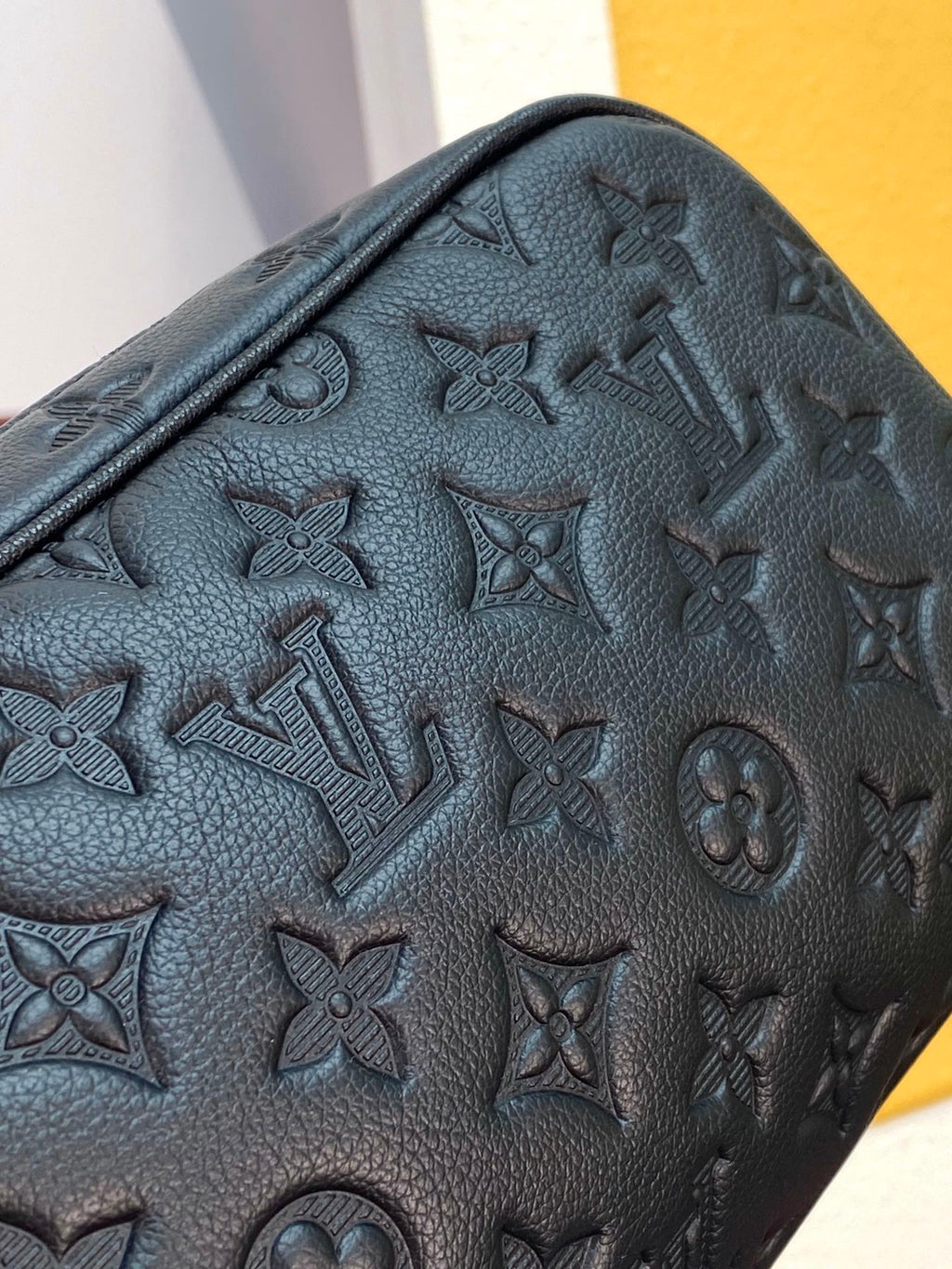 Close-up of monogram toiletry bag side with embossed pattern and textured leather