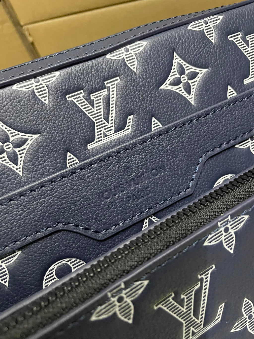 Men's Louis Vuitton bag close-up, navy monogram print and textured leather zipper edge.