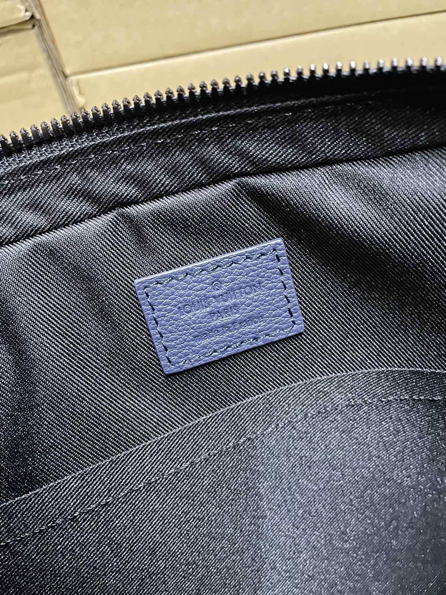 Men's Louis Vuitton bag interior label, blue fabric patch and dark denim lining.