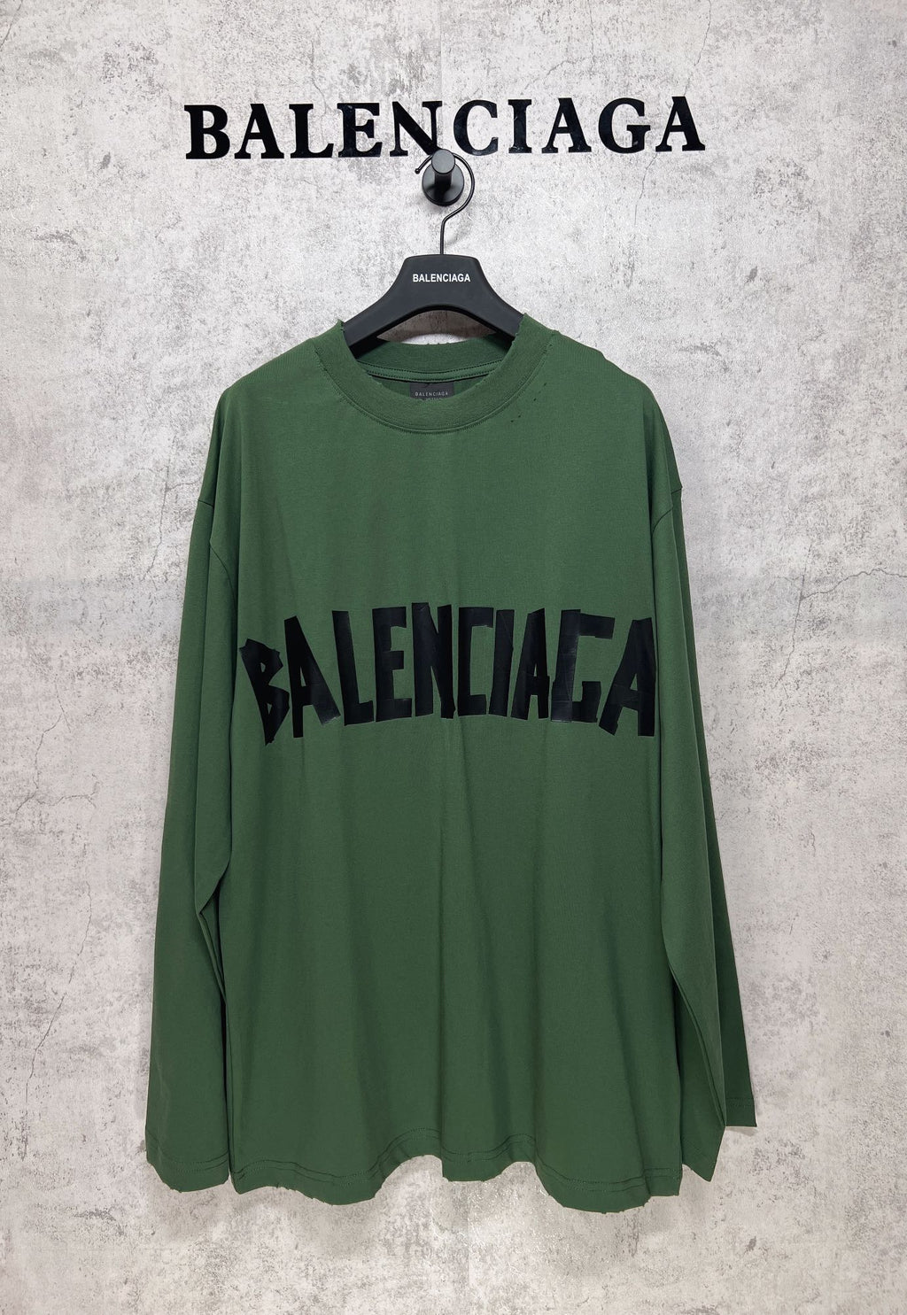 Green long-sleeve T-shirt on hanger with large black Balenciaga logo print