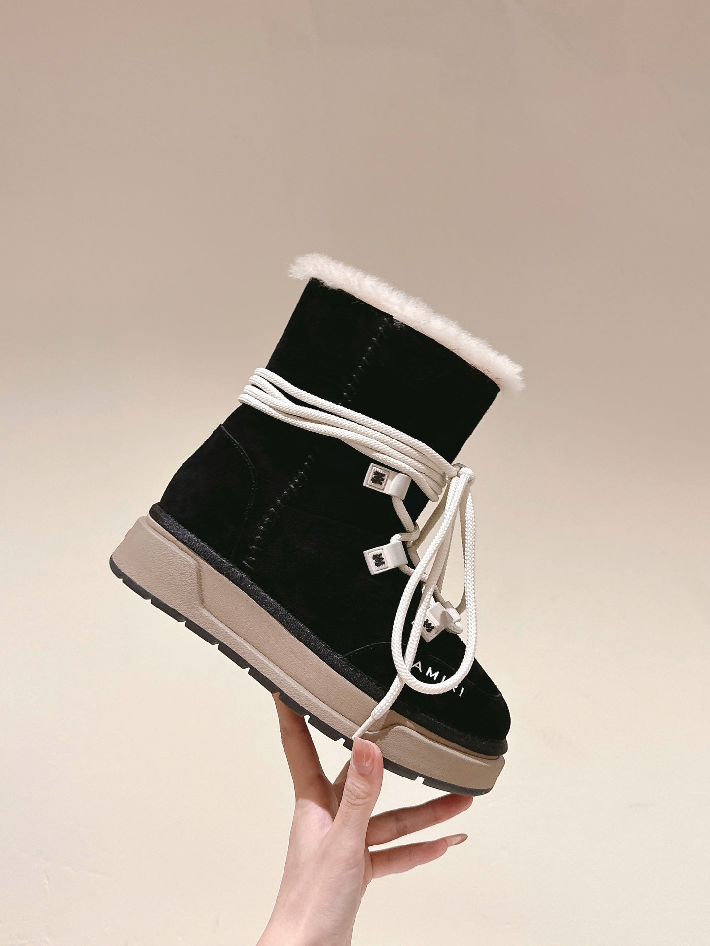 Black high-top boot with white laces and faux-fur cuff, beige sole, angled view.