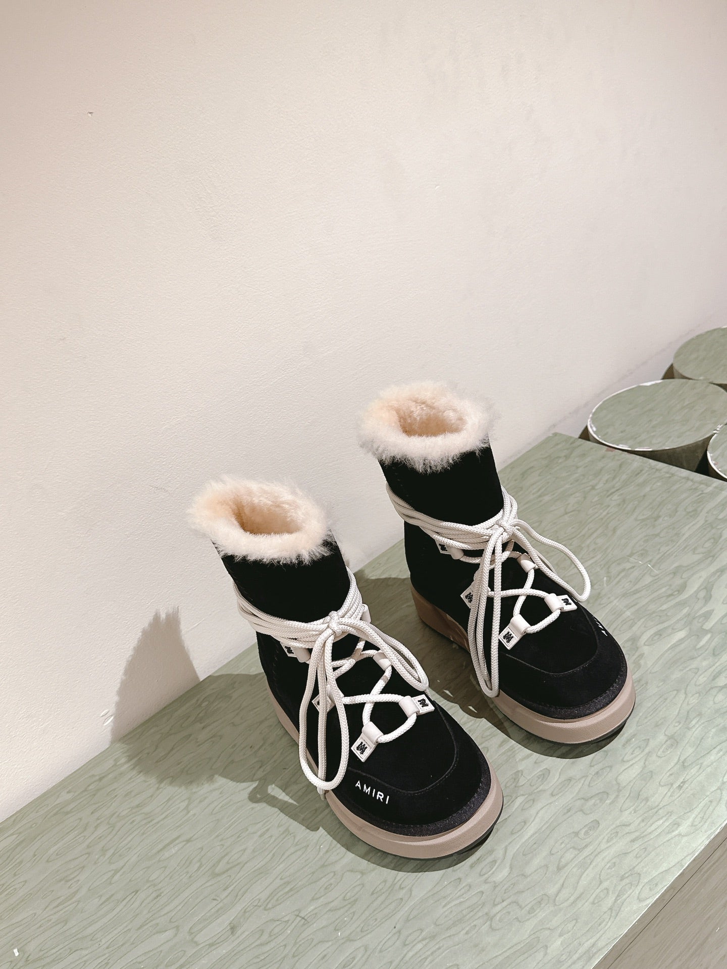 Black high-top lace-up boots with white laces, faux-fur cuffs and beige soles.