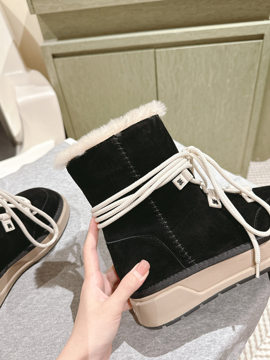 Black lace-up high-top boot with faux-fur collar and white tie laces, beige sole.