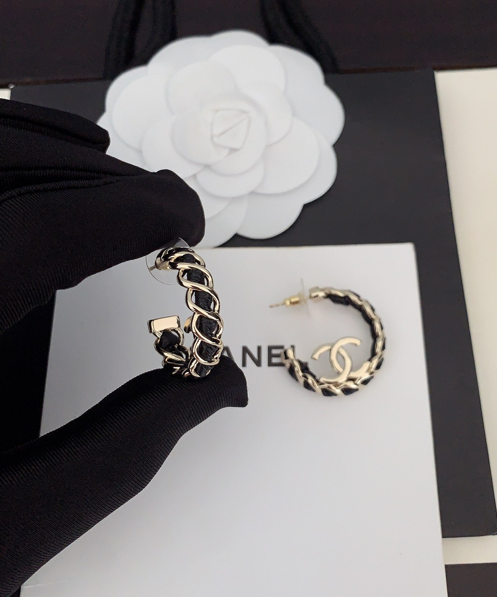 Gold-tone chain hoop earrings with CC logo, held by gloved hand