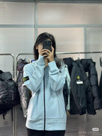 Light blue Stone Island zip-up hoodie with hood and black zipper; sleeve logo patch