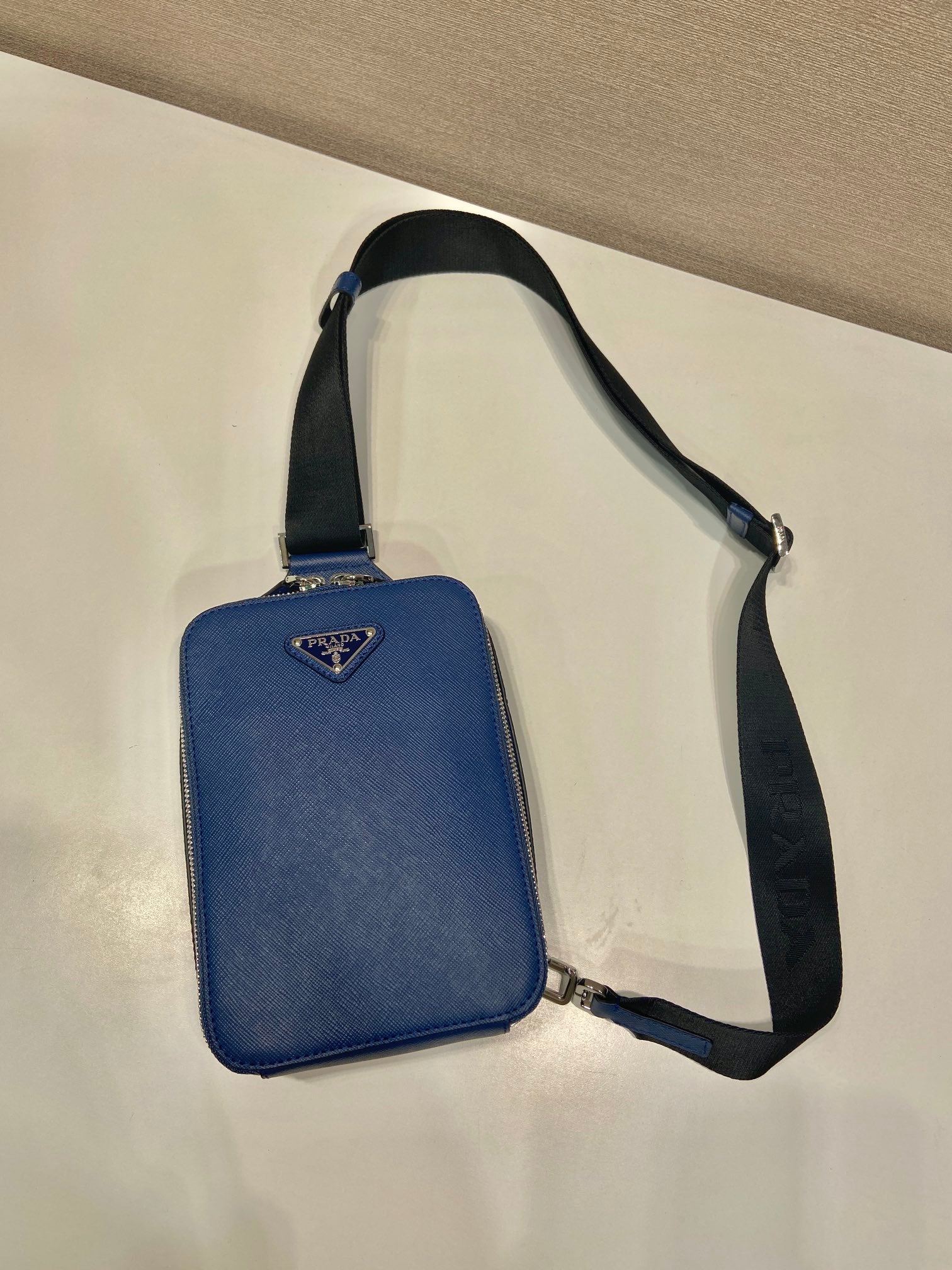 Blue mini crossbody bag with black webbing strap and Prada triangle logo