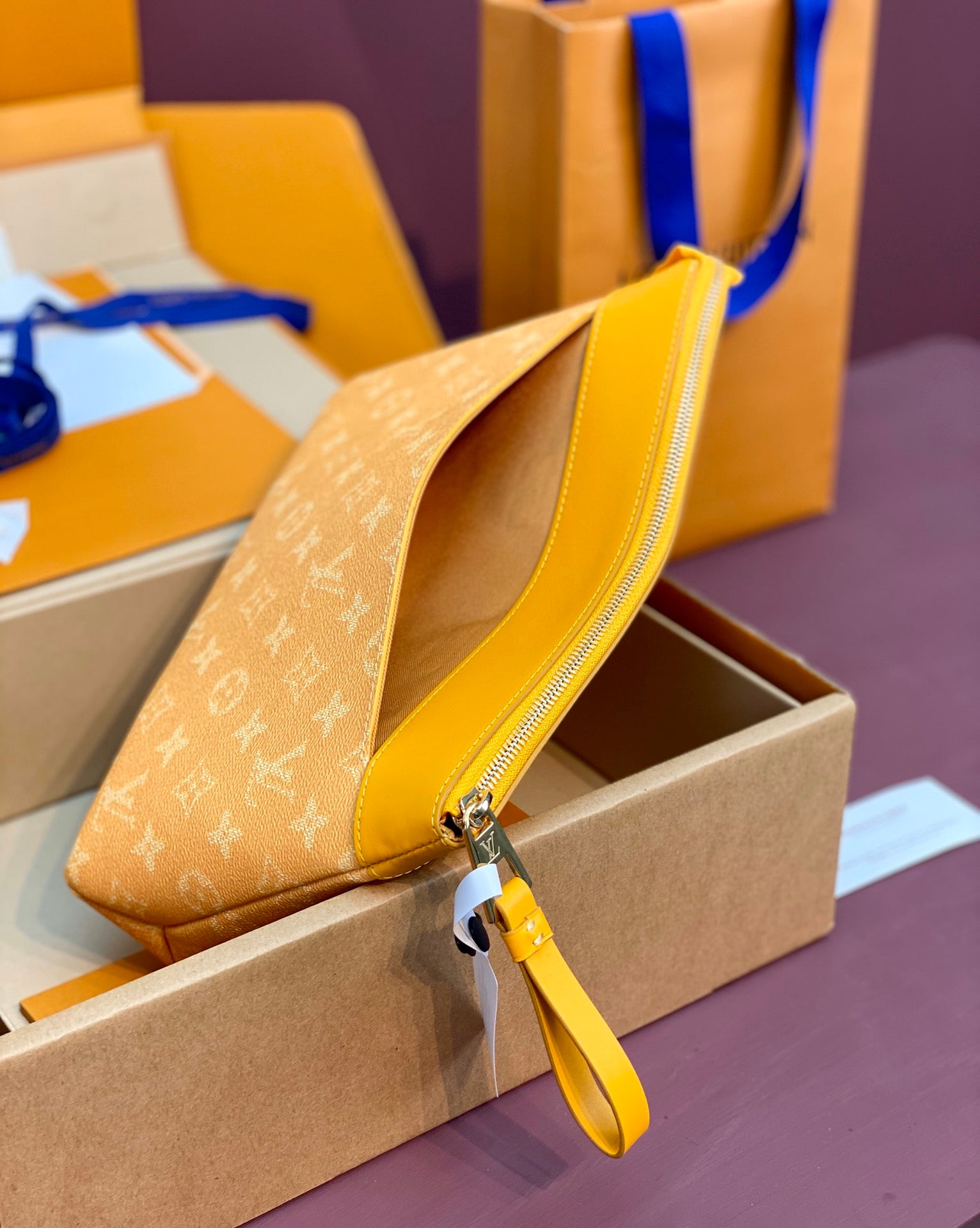 Tan monogram small handbag with blue-edged zipper and strap, resting on box