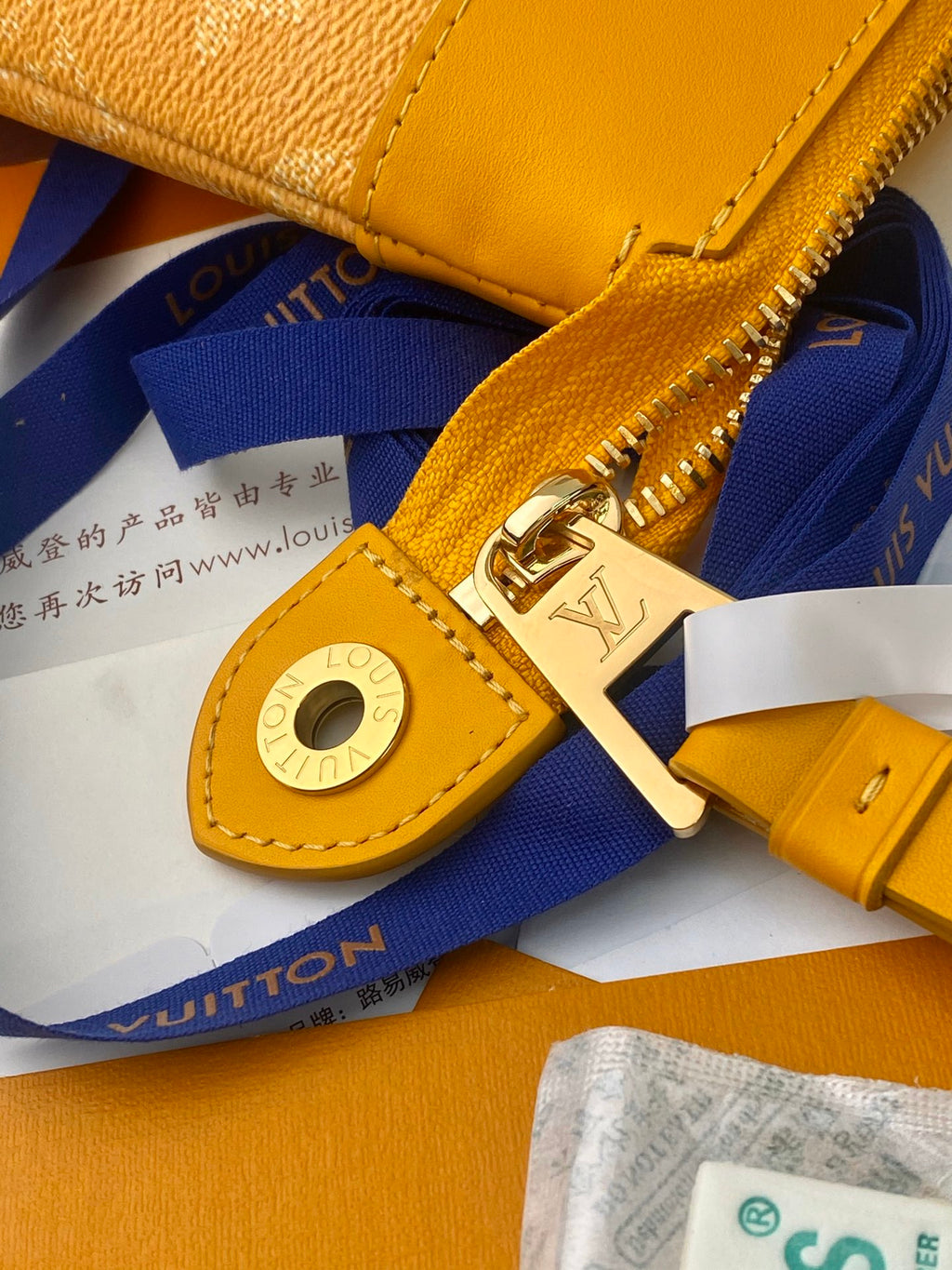Tan monogram handbag close-up of gold zipper pull and circular strap attachment