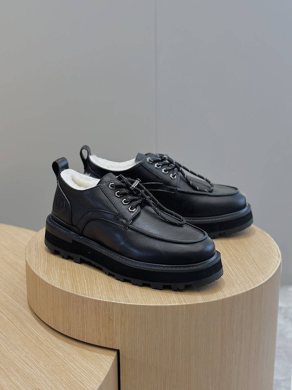 Black leather lace-up shoes on round display, front and side lace detail.