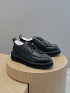 Black leather lace-up shoes on round display, front and side lace detail.