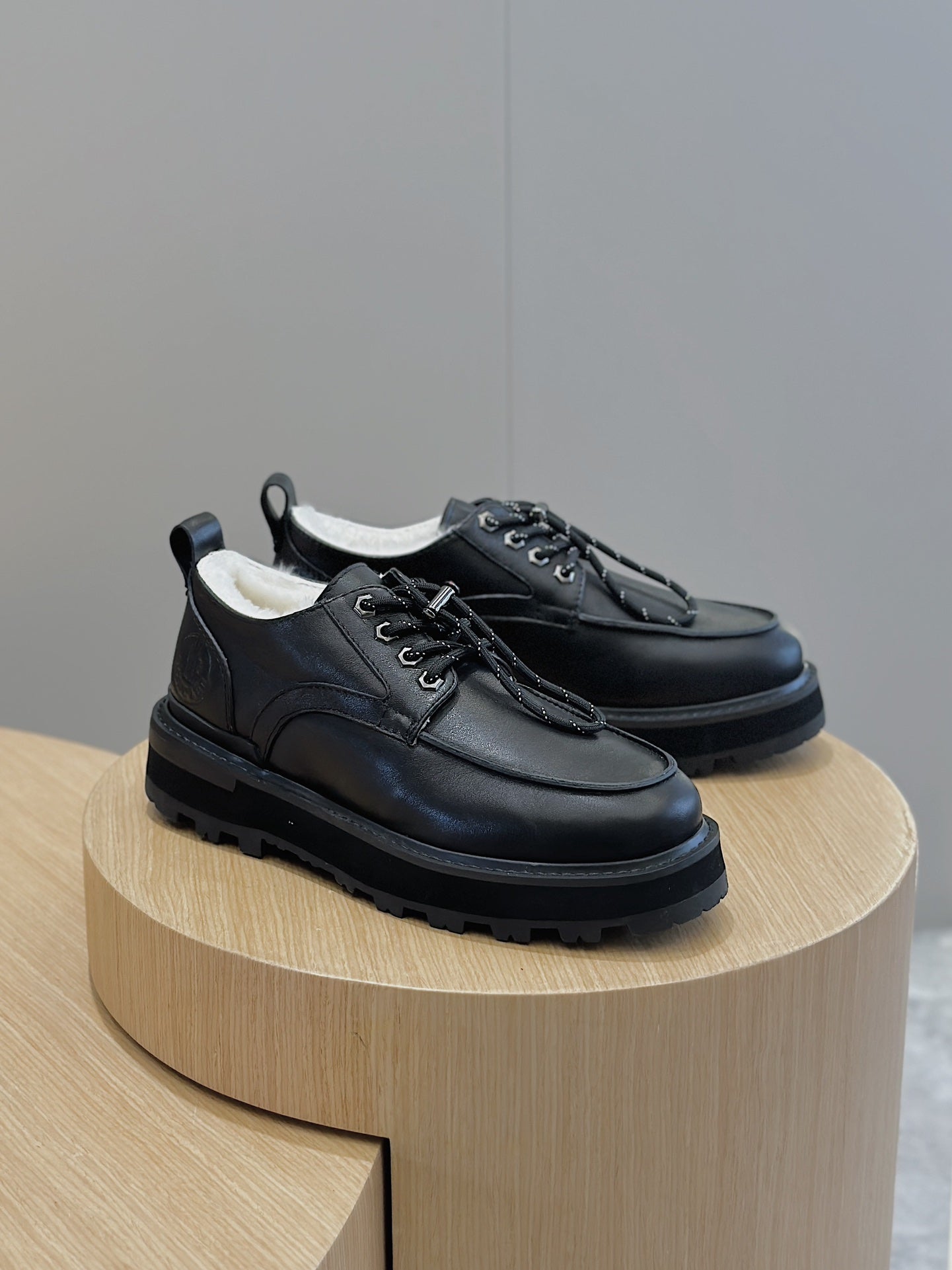 Black leather lace-up shoes on round display, front and side lace detail.
