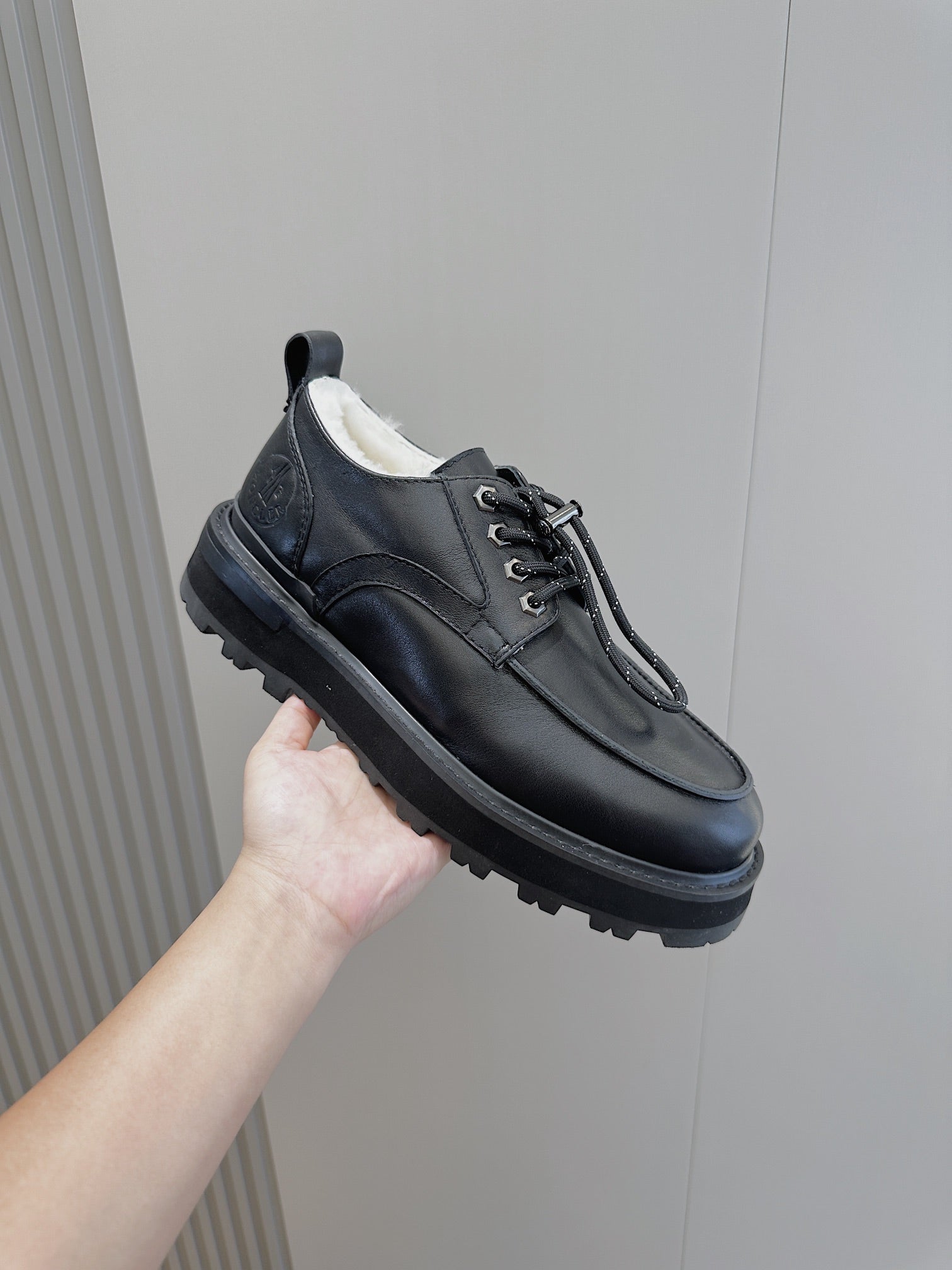 Black leather lace-up shoe held up, low-profile toe and chunky rugged sole.