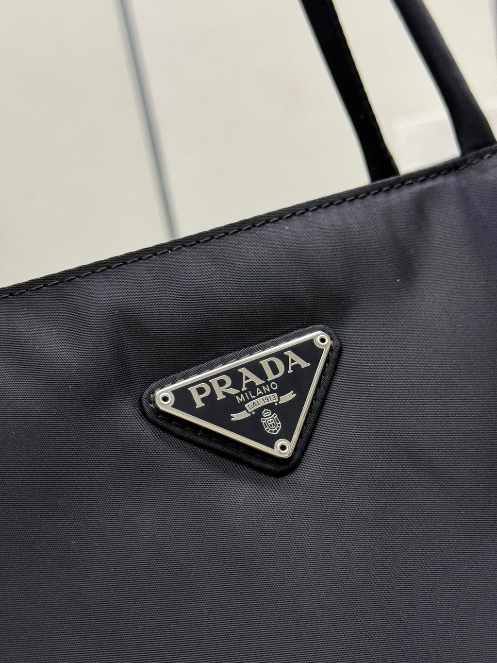 Prada logo patch on black tote bag front with metal-trim border