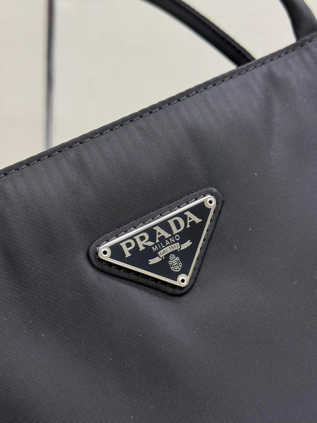 Prada logo patch on dark fabric, triangular metal emblem