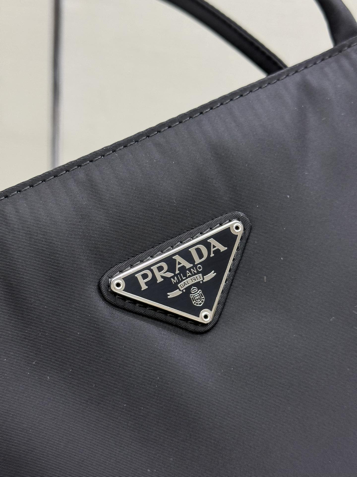 Prada logo patch on dark fabric, triangular metal emblem