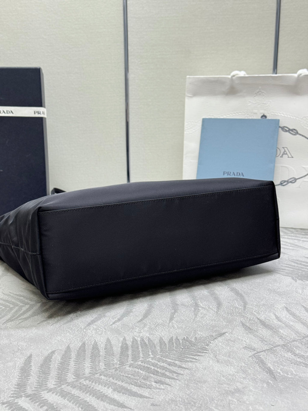 Prada tote bag laid on side, dark fabric with top zipper and handles