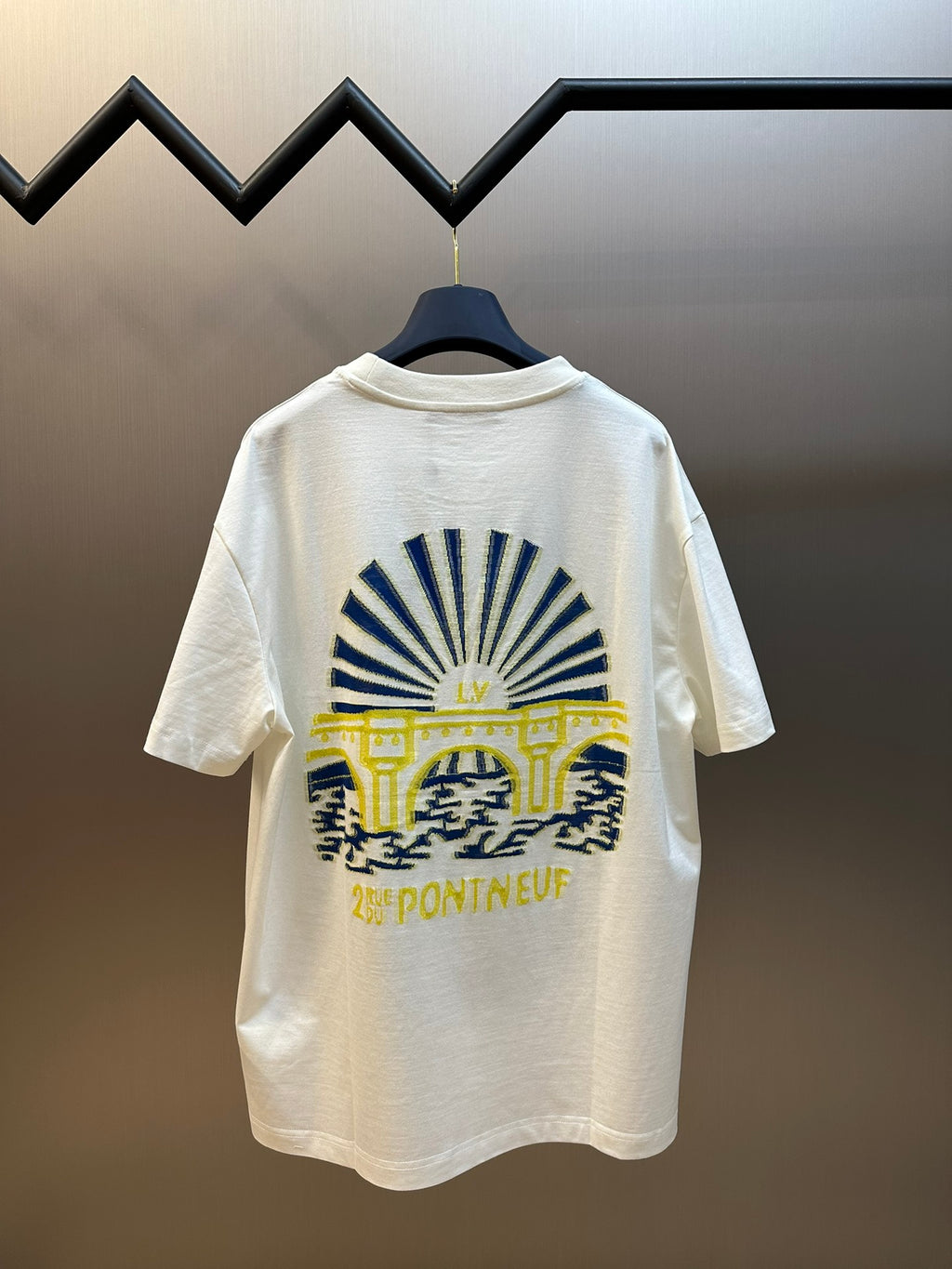 White short-sleeve T-shirt with blue sunburst and yellow-and-blue emblem graphic