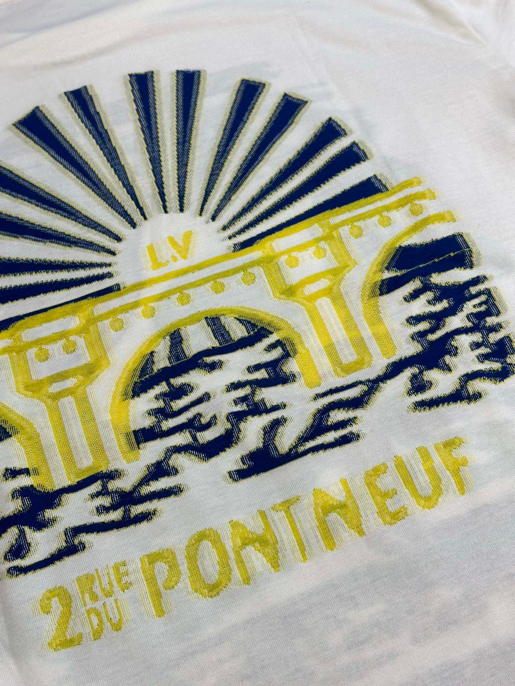 White T-shirt close-up of blue sunburst graphic with yellow text and emblem