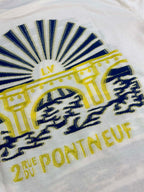 White T-shirt close-up of blue sunburst graphic with yellow text and emblem