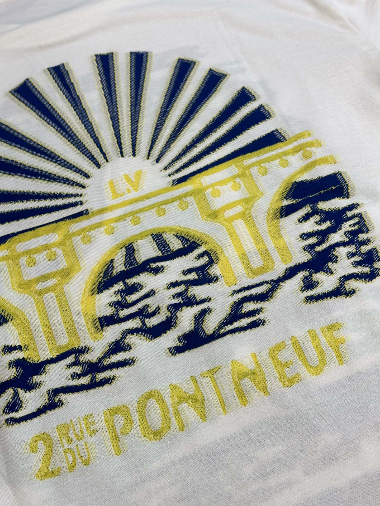 White T-shirt close-up of blue sunburst graphic with yellow text and emblem