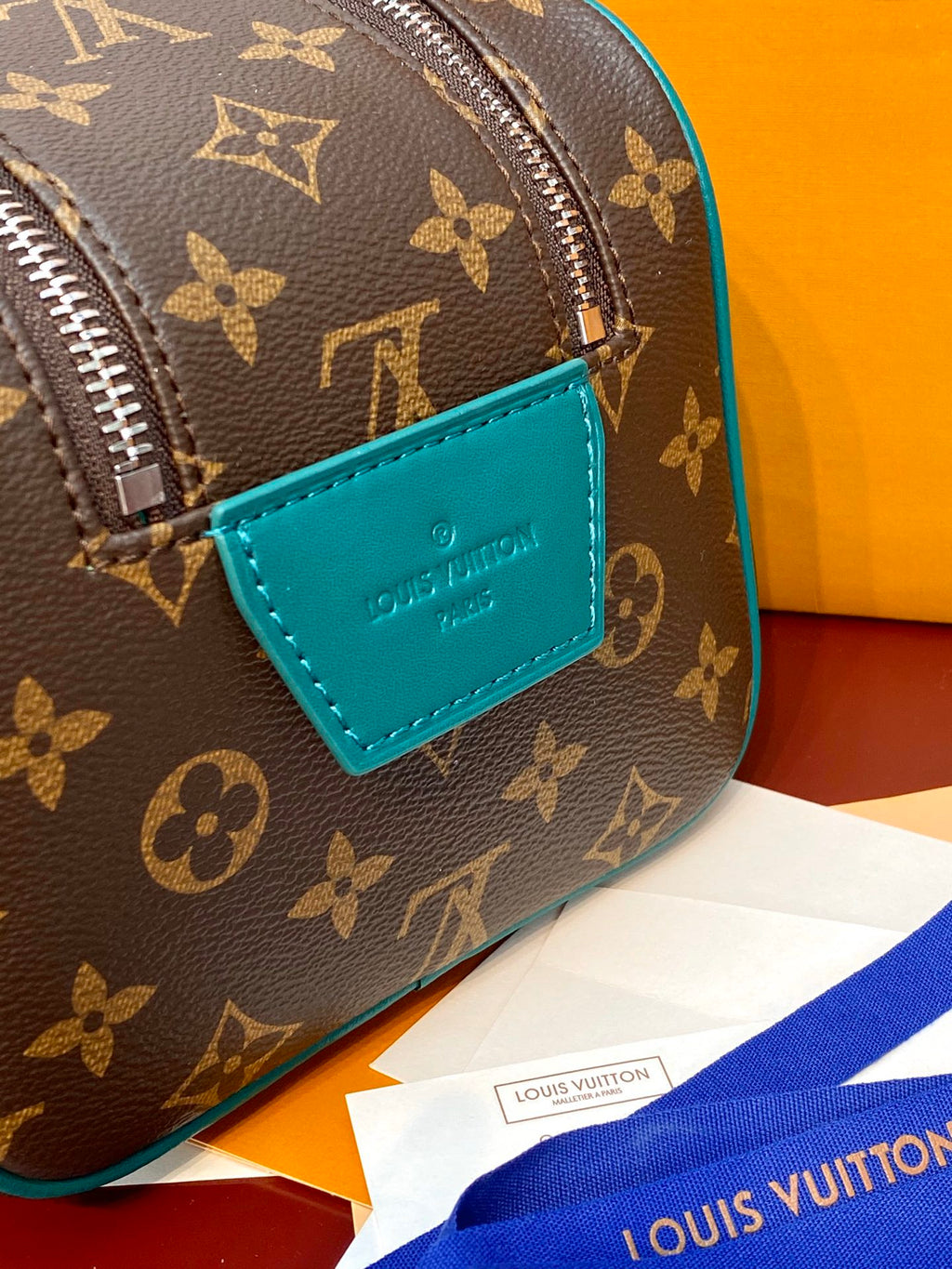 Brown monogram crossbody pouch with teal logo patch and silver zipper