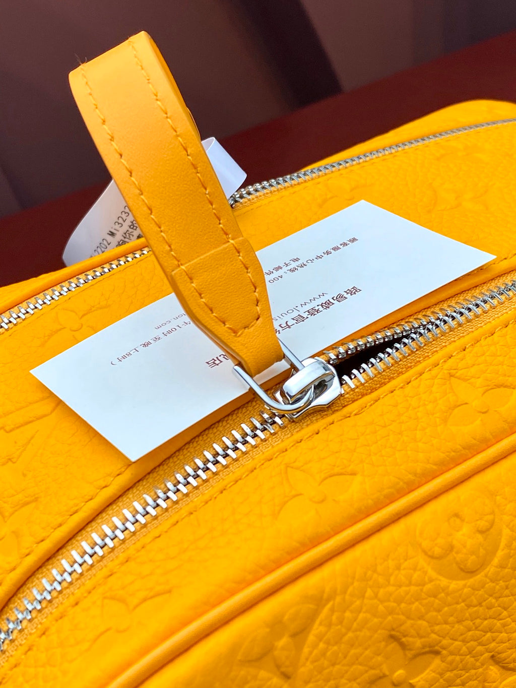 Yellow Louis Vuitton pouch bag close-up of leather strap and metal zipper ring.