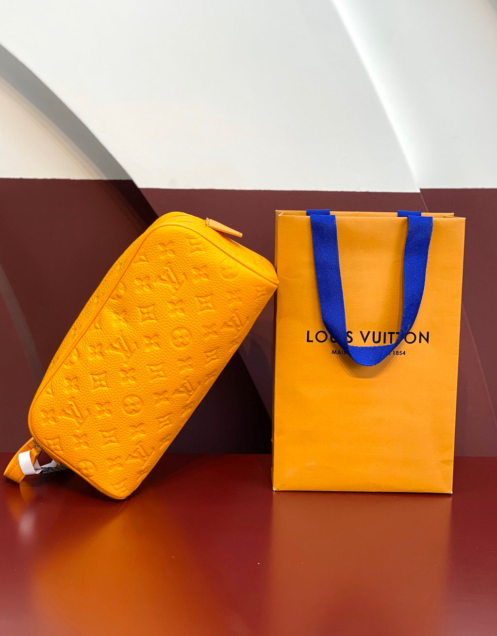 Louis Vuitton yellow crossbody bag with embossed pattern, shown with orange logo shopping bag