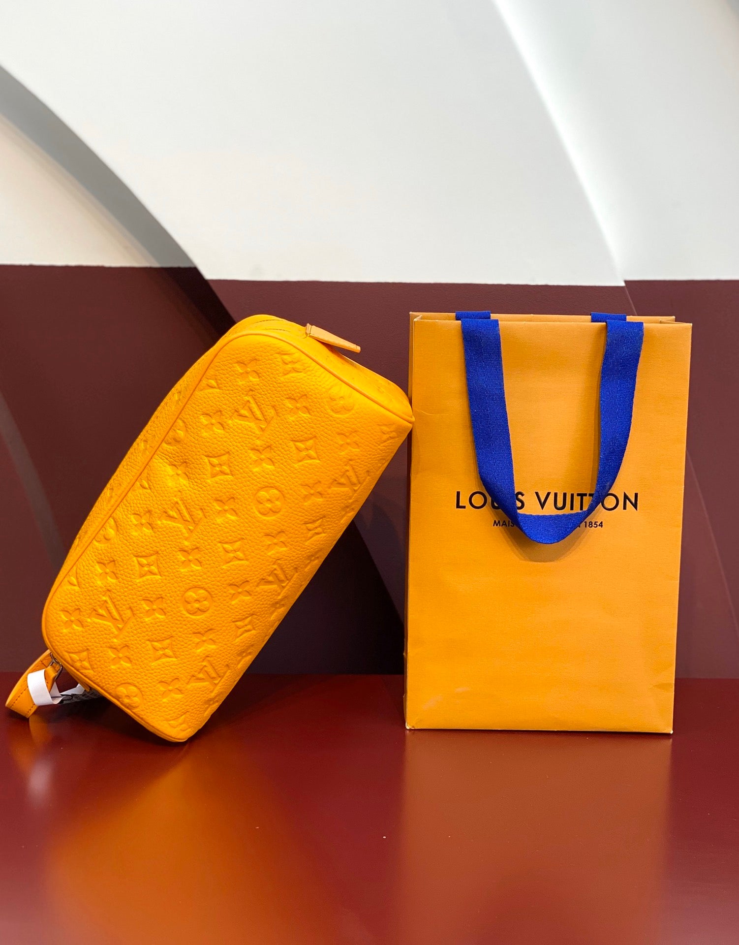 Louis Vuitton yellow crossbody bag with embossed pattern, shown with orange logo shopping bag