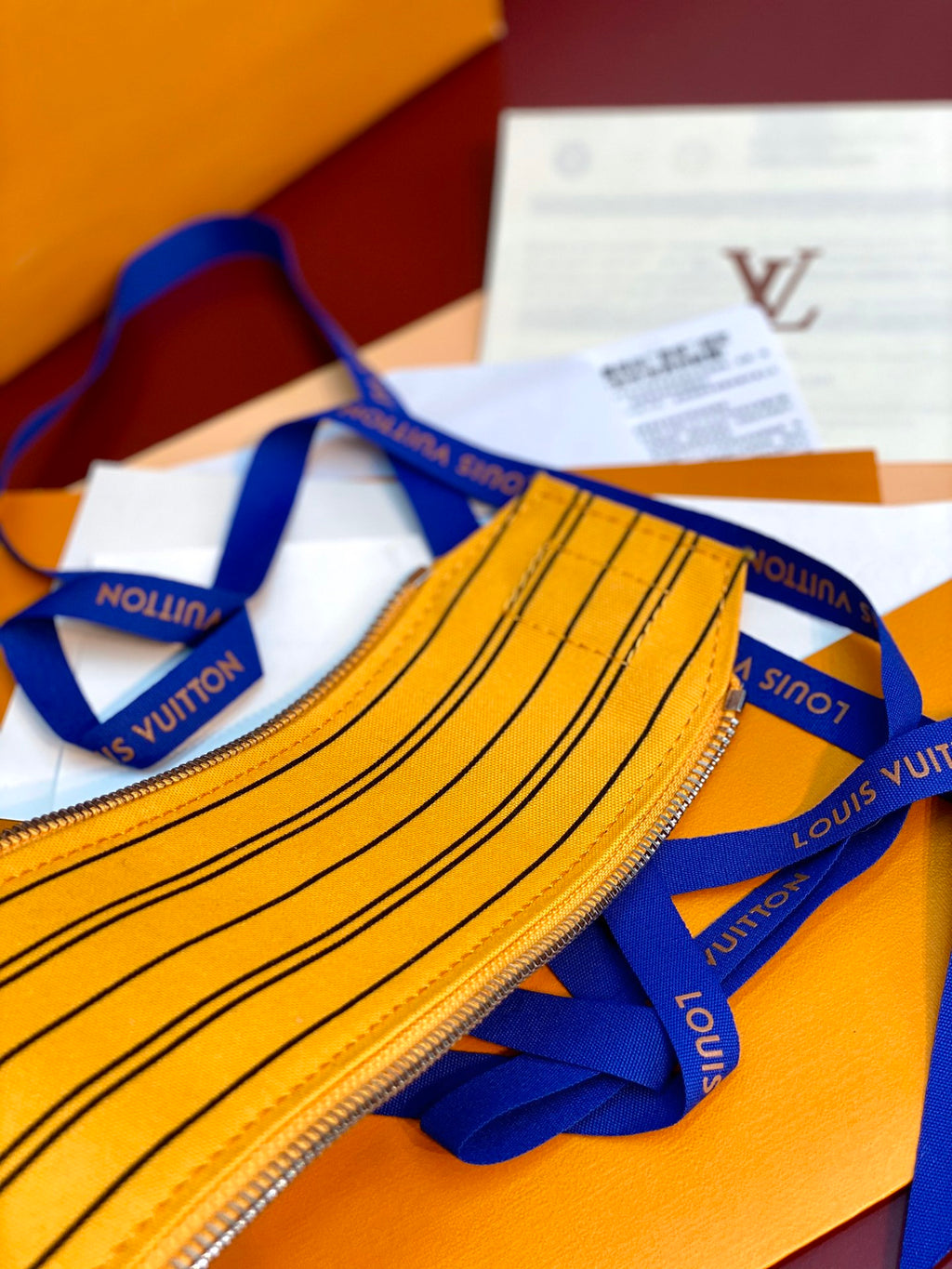 Yellow Louis Vuitton pouch bag front close-up with striped monogram trim and zip.