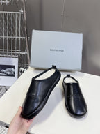 Black leather slide sandals, one hand-held with matching pair