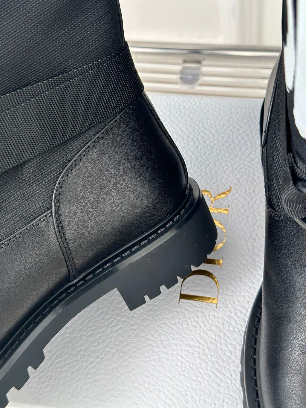 Black leather boot upper with curved stitching, thick lug sole, and panel seams