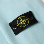Light blue sweatshirt with embroidered yellow circular logo on a black patch