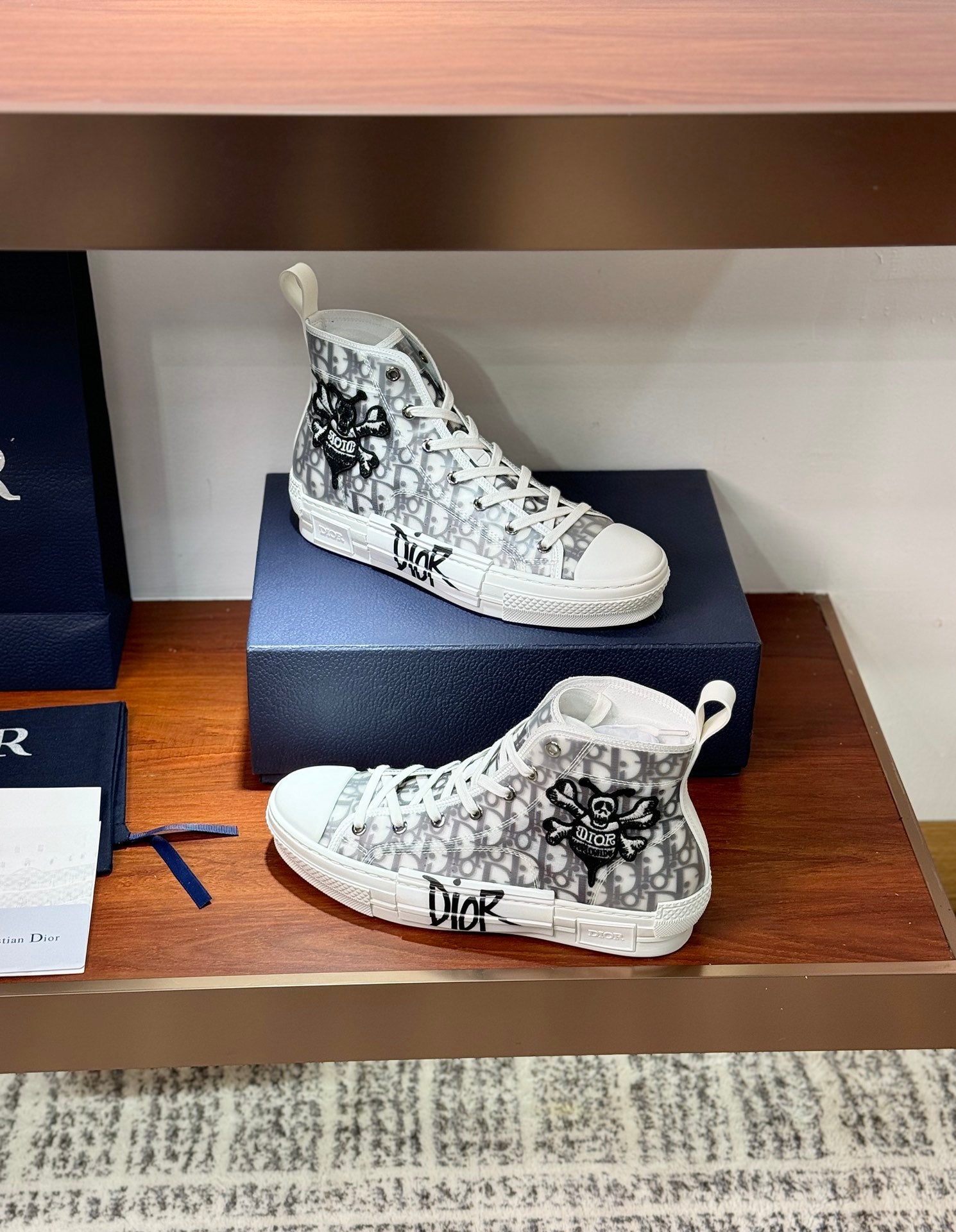 Dior ladies high-top sneakers, white with black monogram pattern, stacked on boxes