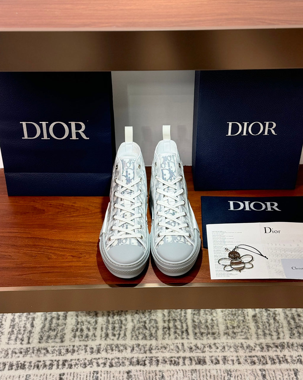 Pair of white high-top sneakers with Dior monogram print and lace-up design.