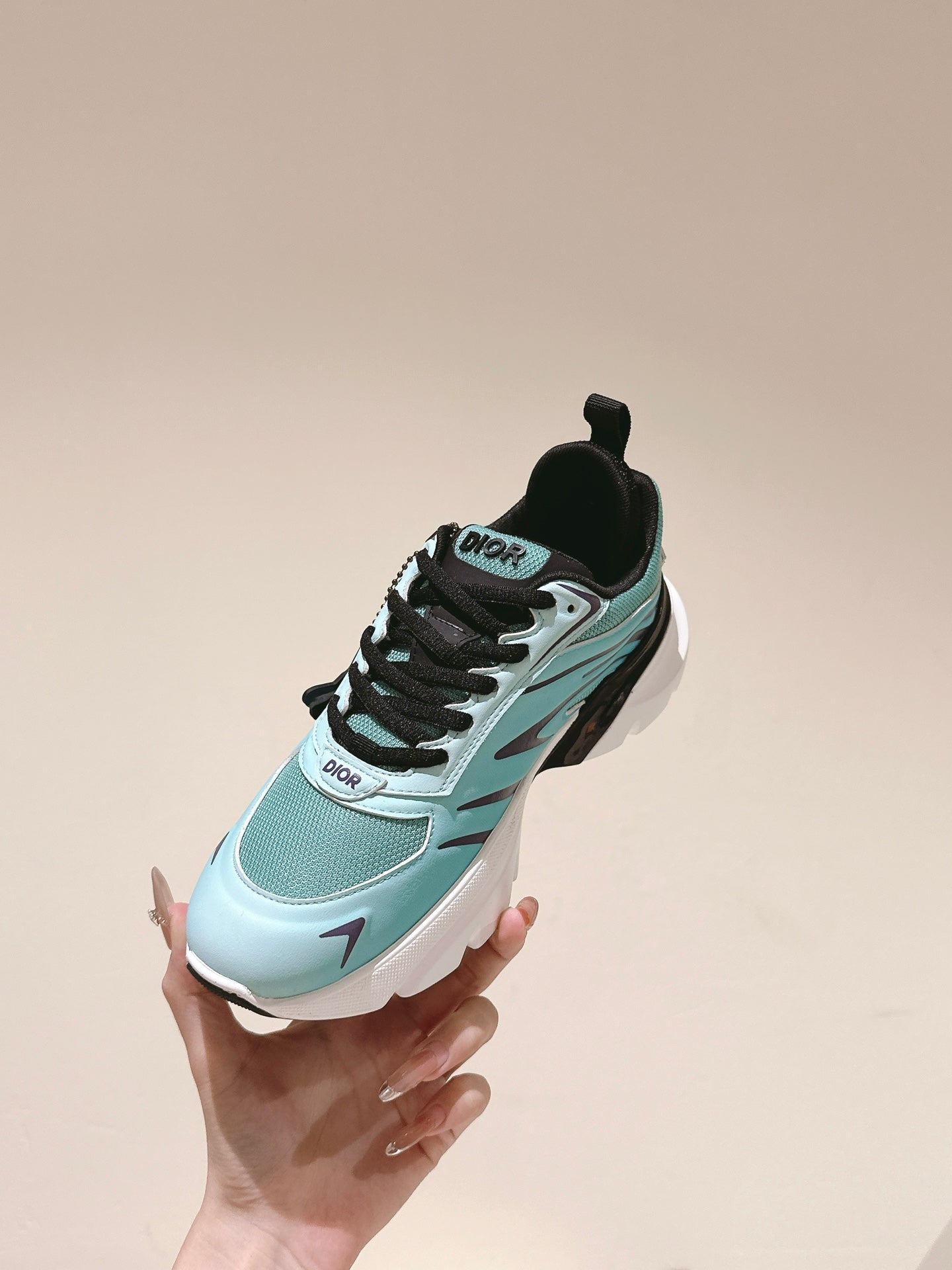 Mint and black sneaker held in hand, side profile with Dior branding and chunky sole