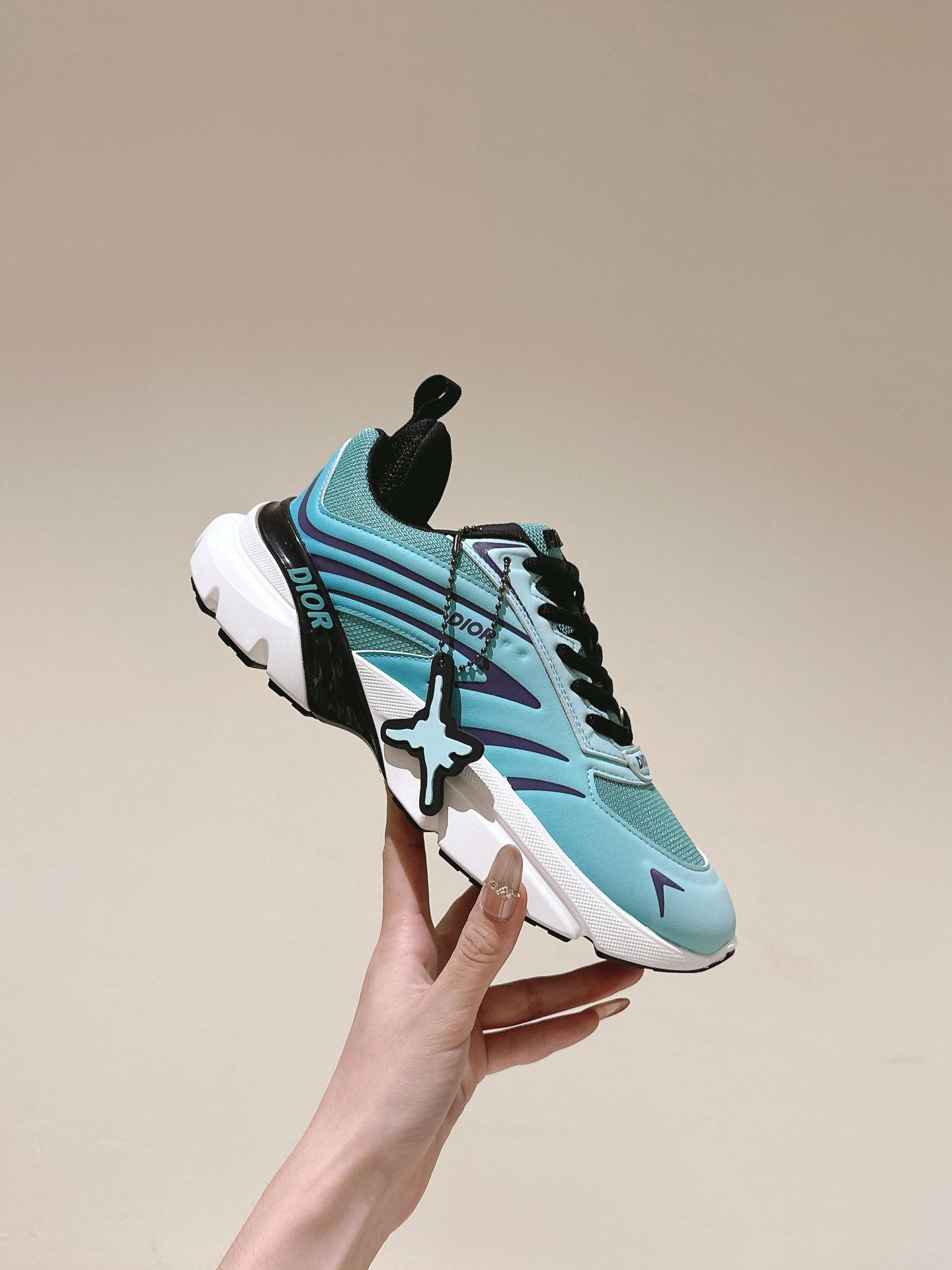 Mint sneaker held in hand showing side logo, black laces, and white sole